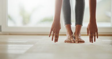 person's-legs-standing-on-yoga-mat-while-fingertips-touching-mat-in-forward-fold-doing-yoga-at-home