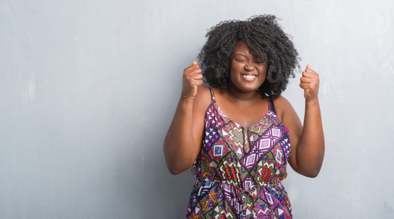 young-plus-size-woman-wearing-purple-patterned-dress-doing-happy-fist-pump-gesture