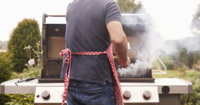 man-facing-away-from-camera-standing-at-gas-grill-cooking-food