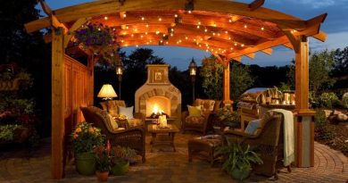 A backyard patio with mosquito repellents under a wooden structure lit by fairy lights and a wood fire stove