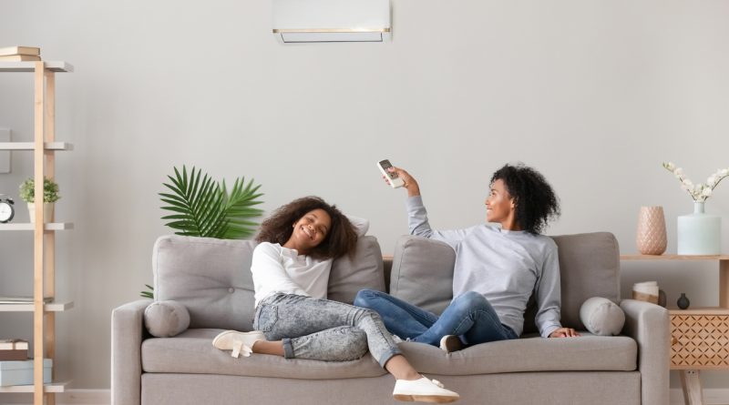 A mother and daughter sitting on a couch in a living room under a ductless mini split air conditioner wall unit