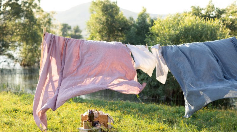 Purple and blue bed sheets hanging on a clothesline in a sunny yard with a breeze.