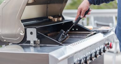 A person's arm scraping a gas grill grate with a grill brush.