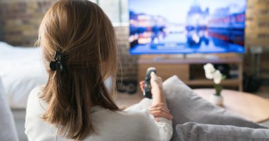 A woman using a remote control to change the channel on an LCD TV on the other side of the room while she sits on a couch.