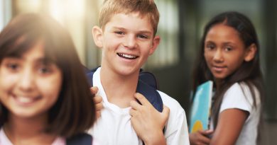 A middle school boy with a backpack smiling while standing in line with other students.