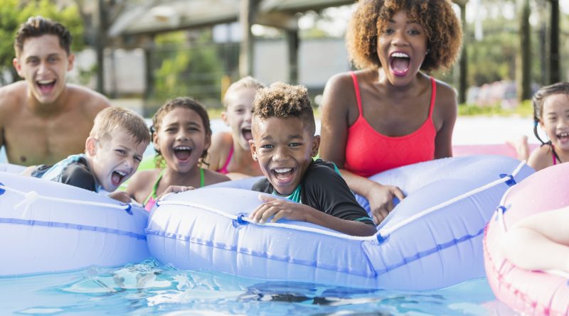 A group of kids with two adults in a lazy river at a water park with inner tubes.