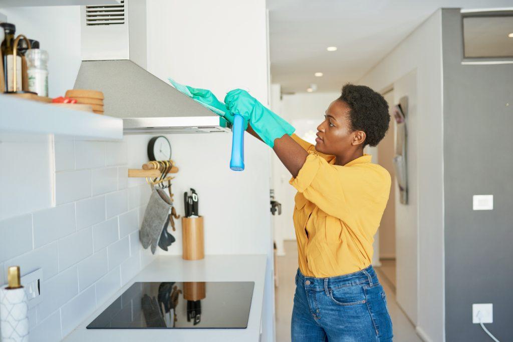 a woman cleaning the exterior of a kitchen range hood