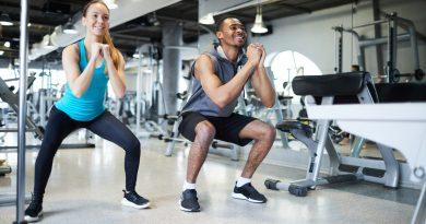 Man and woman in a gym performing squat exercises and using the Row-N-Ride Trainer for more manageable routines.