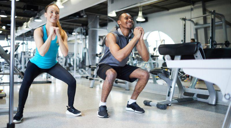 Man and woman in a gym performing squat exercises and using the Row-N-Ride Trainer for more manageable routines.