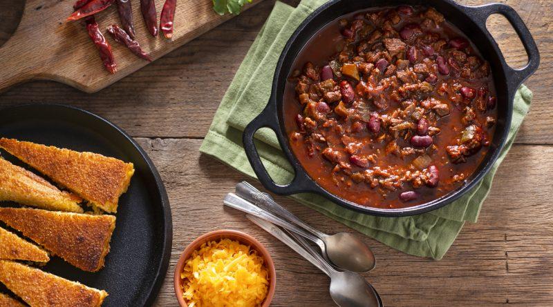 Classic chili inside of a cast iron Dutch oven on top of a table with other ingredients.