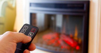 A person operating an electric fireplace at home using a remote control.