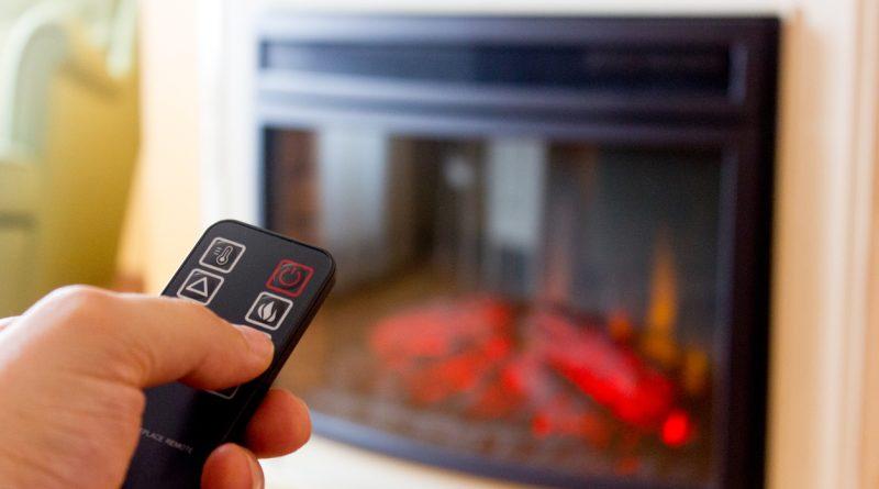 A person operating an electric fireplace at home using a remote control.